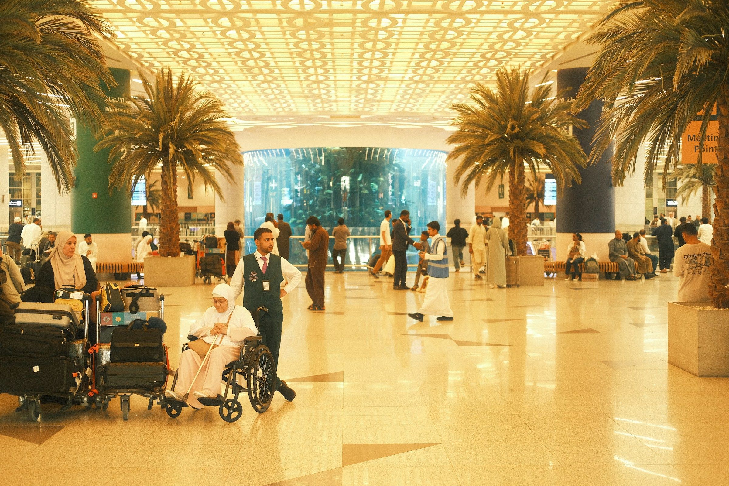 Travellers, luggage trolleys and wheelchair assistance in the arrivals hall at Jeddah airport